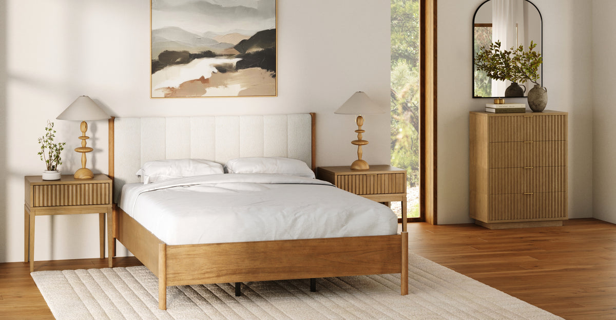 A bedroom featuring a wooden bed frame, two matching nightstands with lamps, and a tall chest of drawers with a mirror above it.
