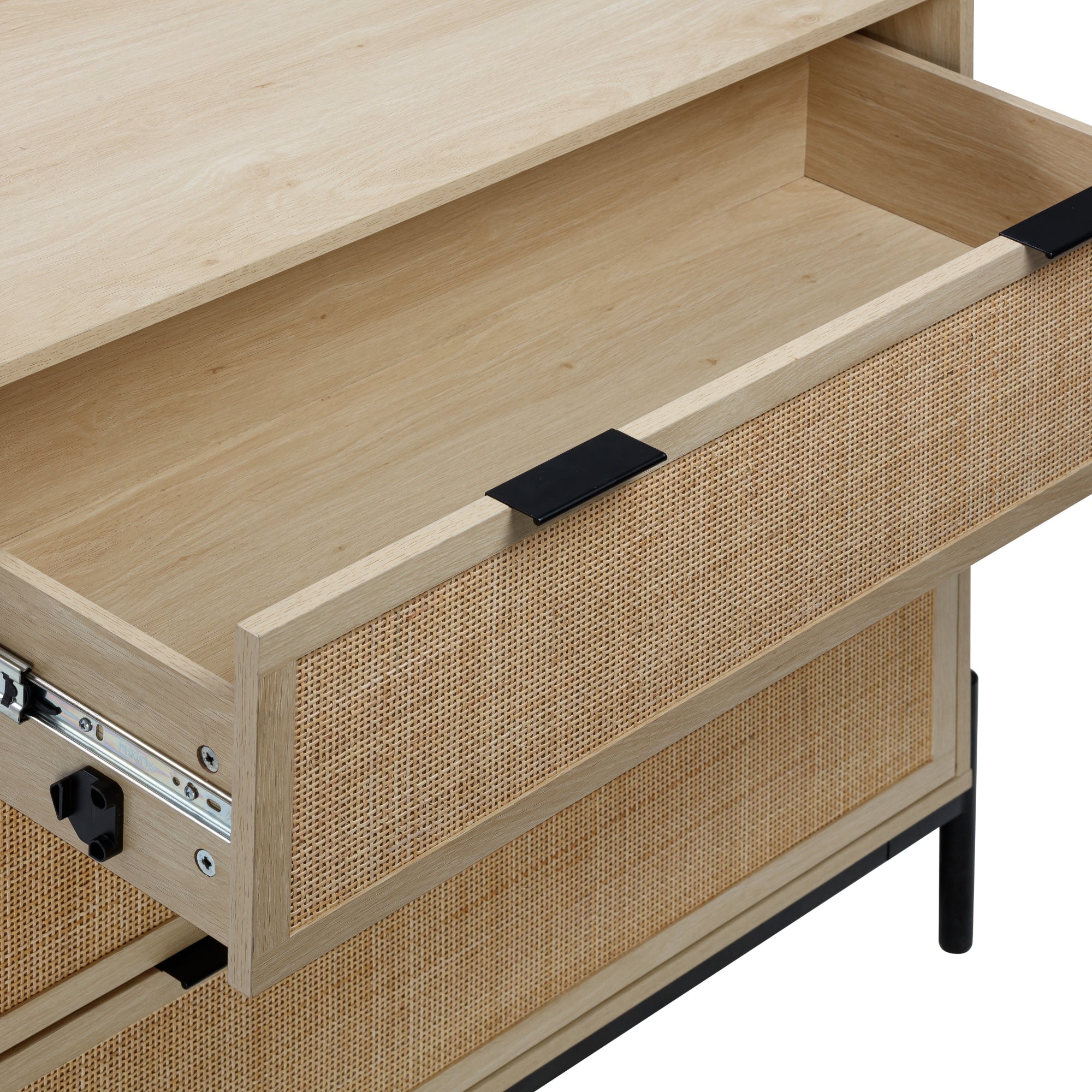 A close-up of an open wooden drawer with a light wood finish and woven rattan front, revealing an empty interior. The furniture has black metal legs and hardware.