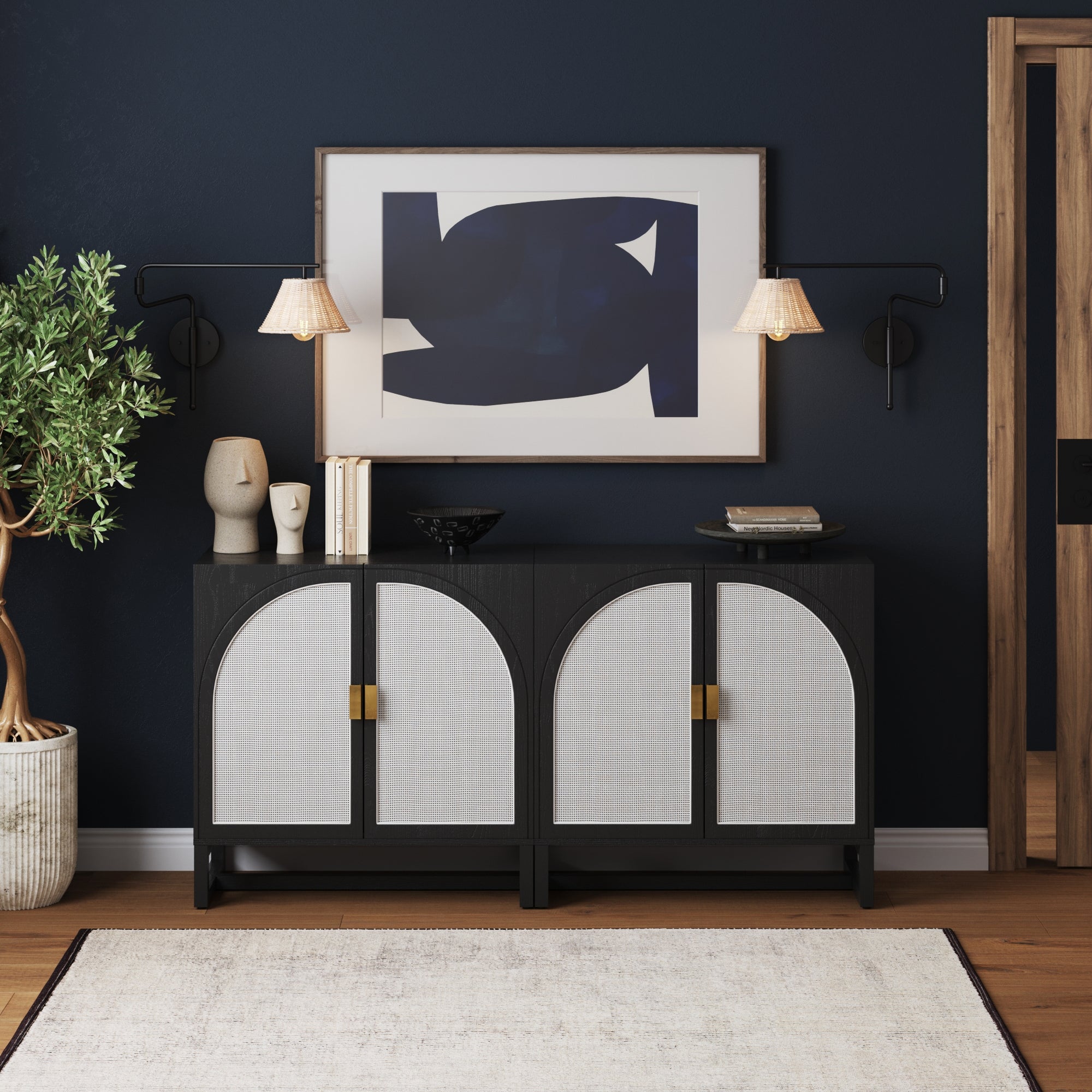 The Nathan James Rattan Arched TV Console Credenza Black (Set of 2) stands against a dark blue wall, adorned with decor, books, and art. Above hang a large abstract painting and two wall lamps, with a potted plant next to the credenza.