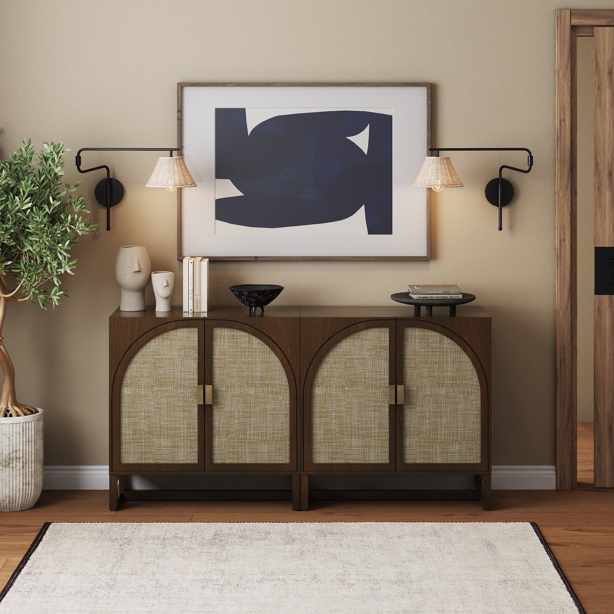 A modern console table with arched doors holds decorative vases, books, and bowls. Above, a large abstract artwork hangs on a beige wall, flanked by two wall-mounted lamps. An indoor plant sits to the left.