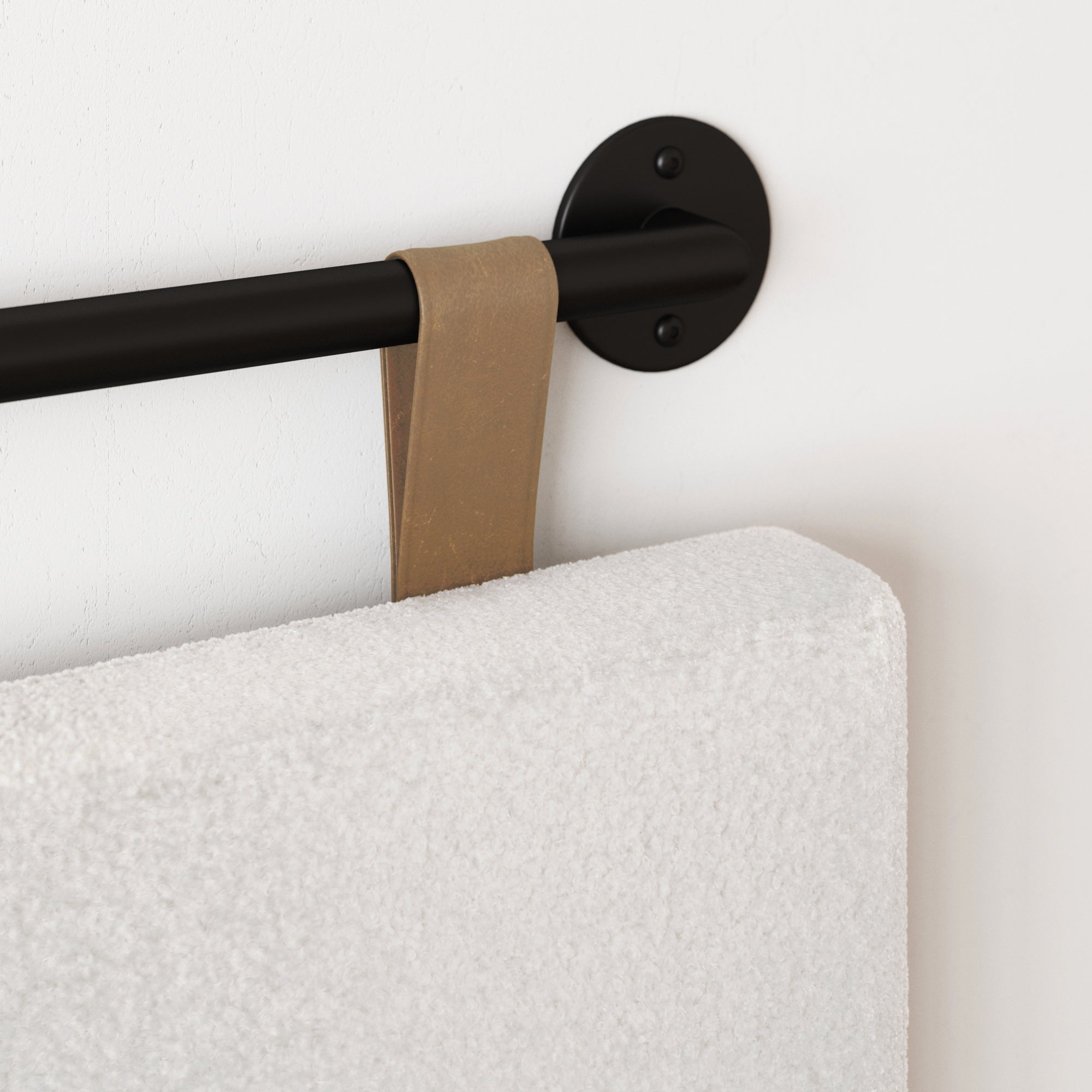 A close-up of a black rod mounted on a white wall with a light brown leather loop holding a thick, white textured cushion or mat.