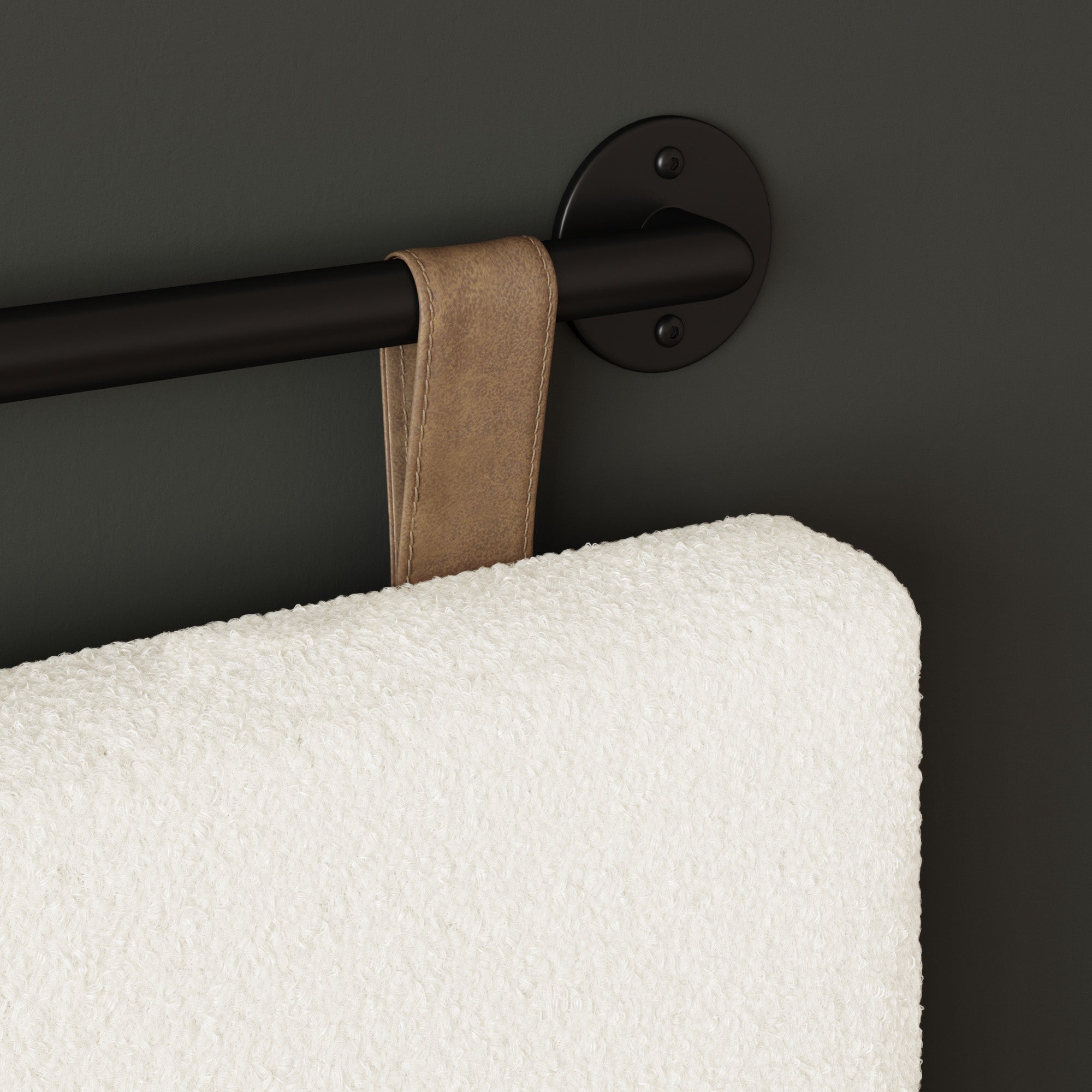 A close-up of a white textured towel with a brown loop hanging on a black wall-mounted towel bar against a dark gray wall.