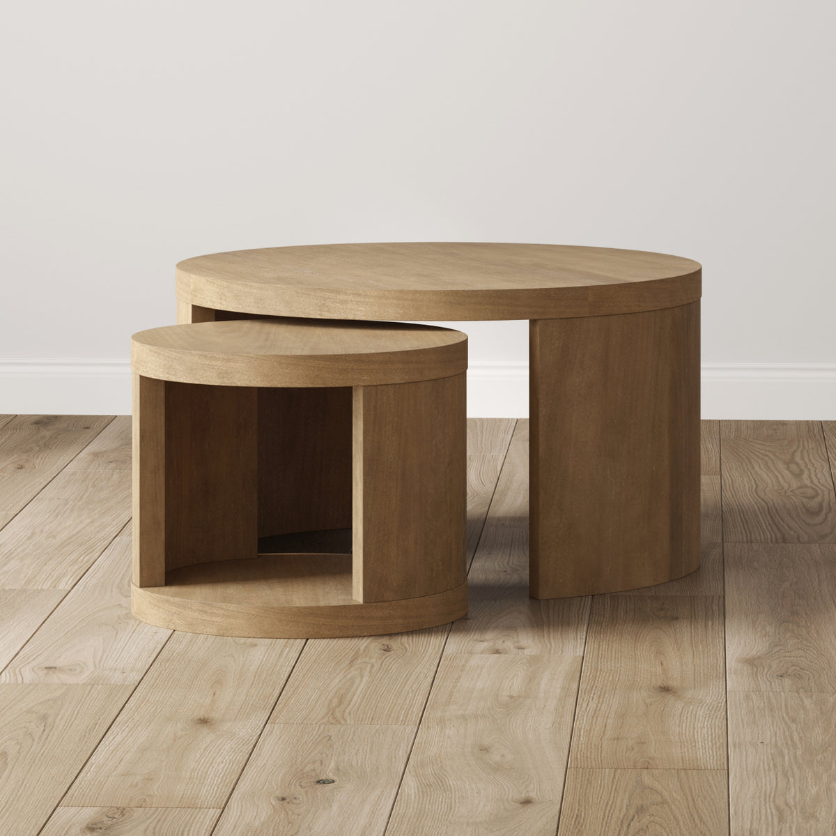 Two circular wooden nesting tables on a wood floor.