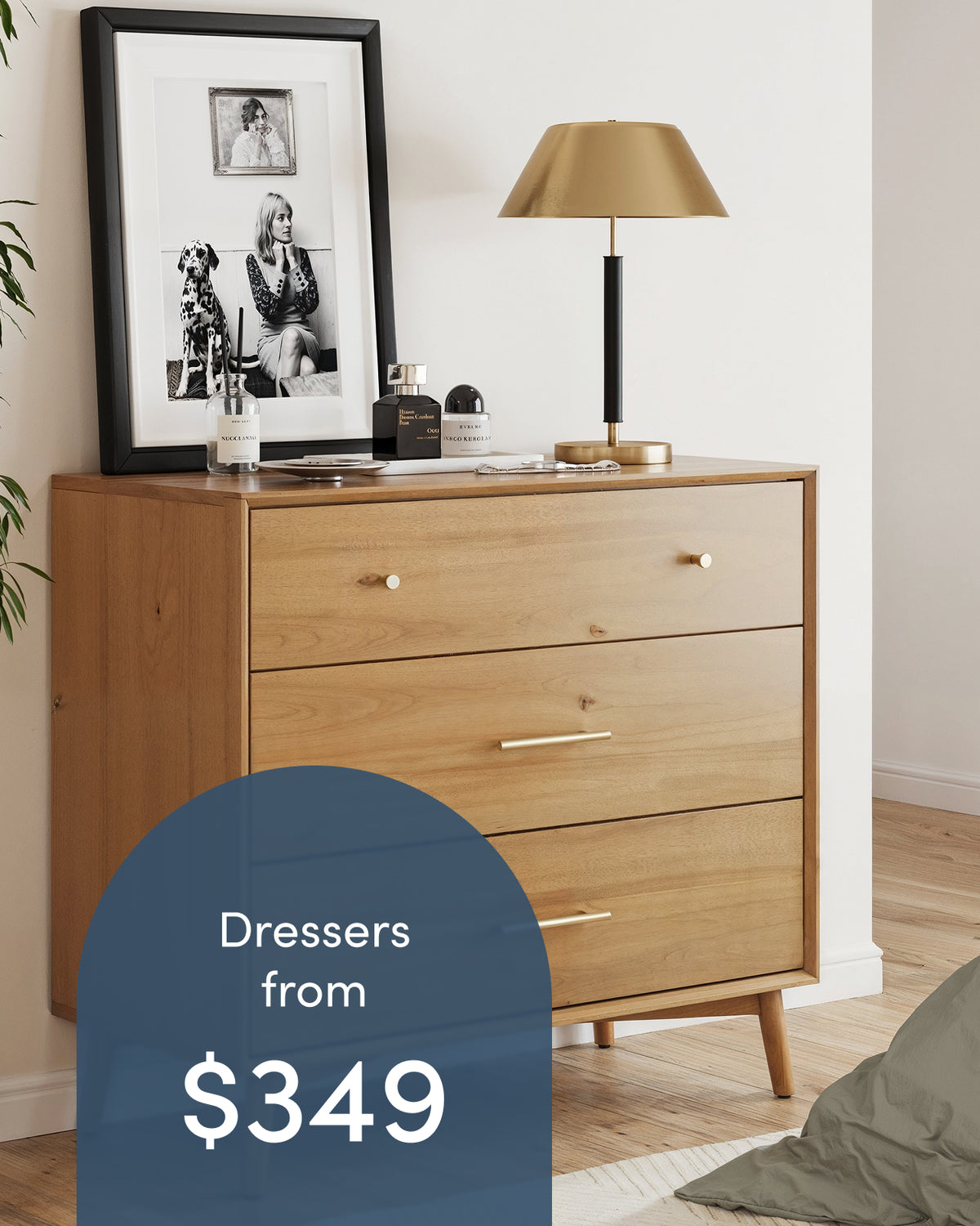 A wooden three-drawer dresser topped with a framed photograph, two perfume bottles, and a gold desk lamp, overlaid with text reading Dressers from $349.