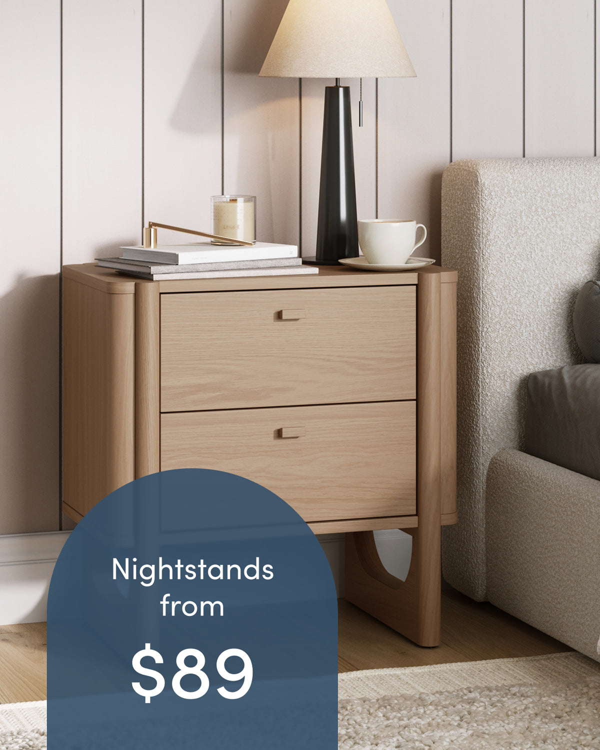 Light wood two-drawer nightstand with a lamp, candle, and coffee cup on top, with overlay text reading Nightstands from $89.