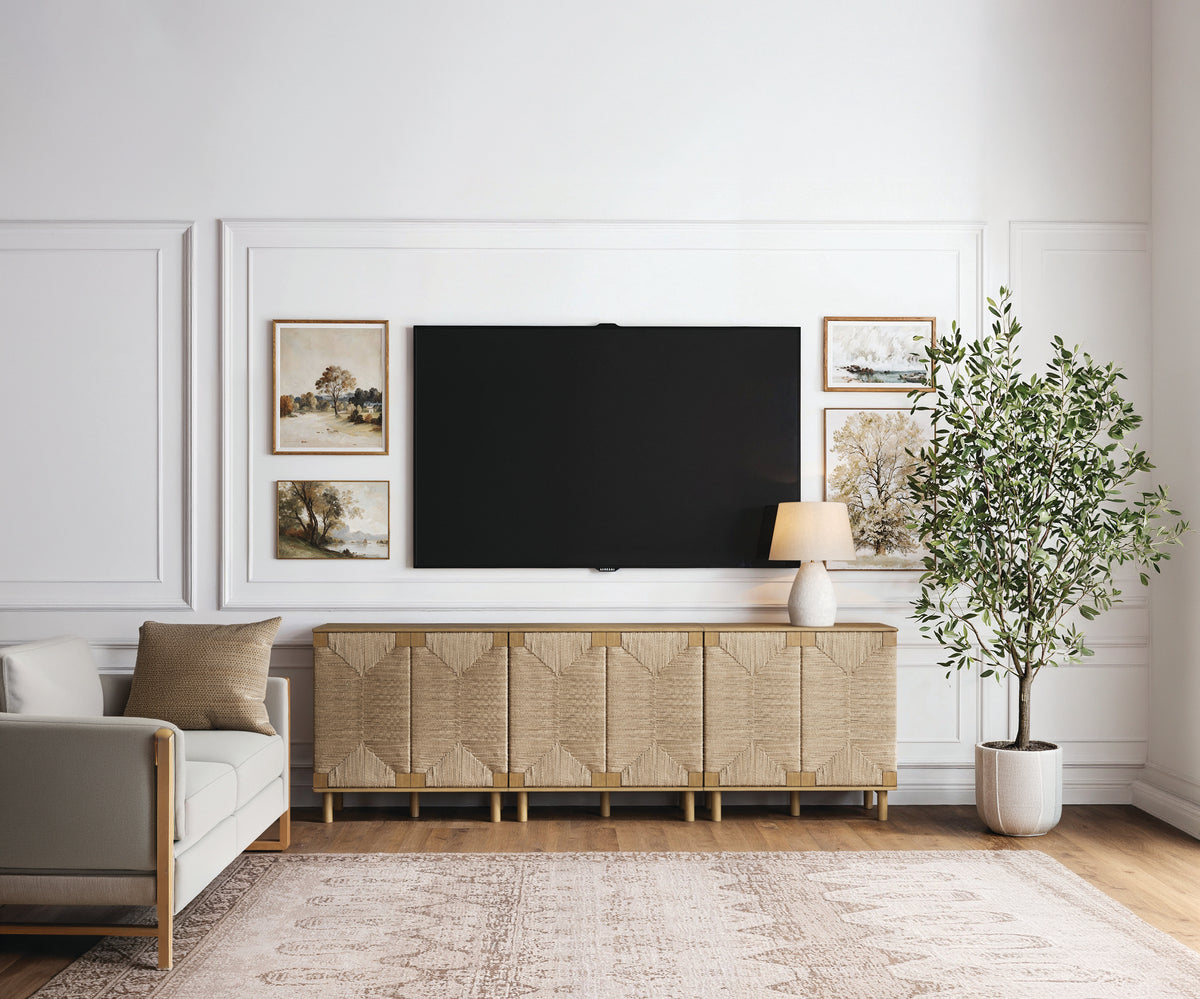 A large flat-screen television hangs above a wide, textured wooden media console, flanked by framed landscape prints and a potted indoor tree in a living room.
