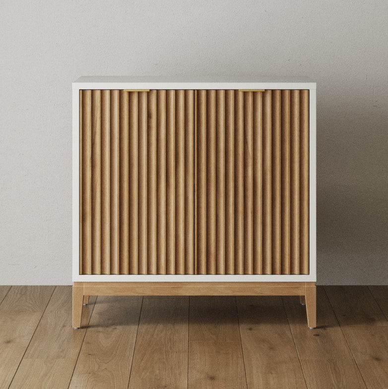 White cabinet with two fluted wood doors, brass pulls, and light wood legs.