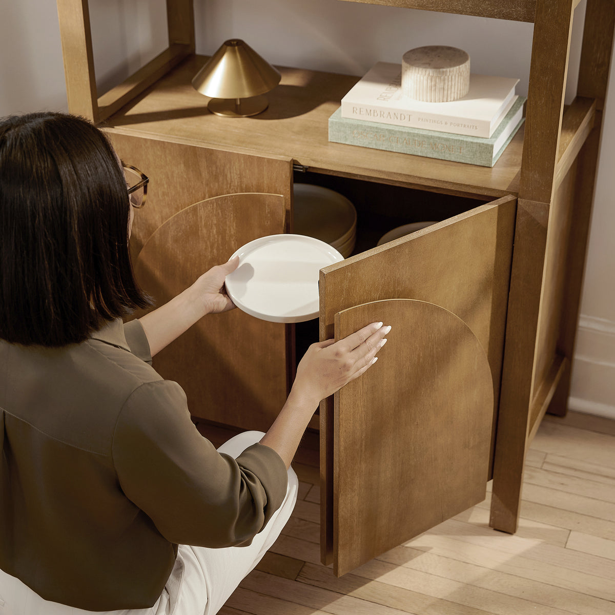 A person placing a white plate into a wooden cabinet.