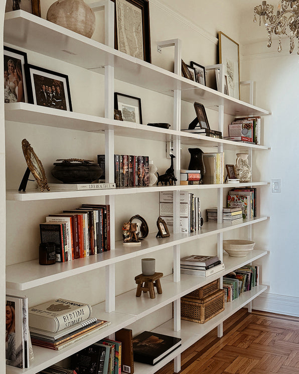 A floor-to-ceiling white bookshelf filled with books, framed photos, and decorative objects.