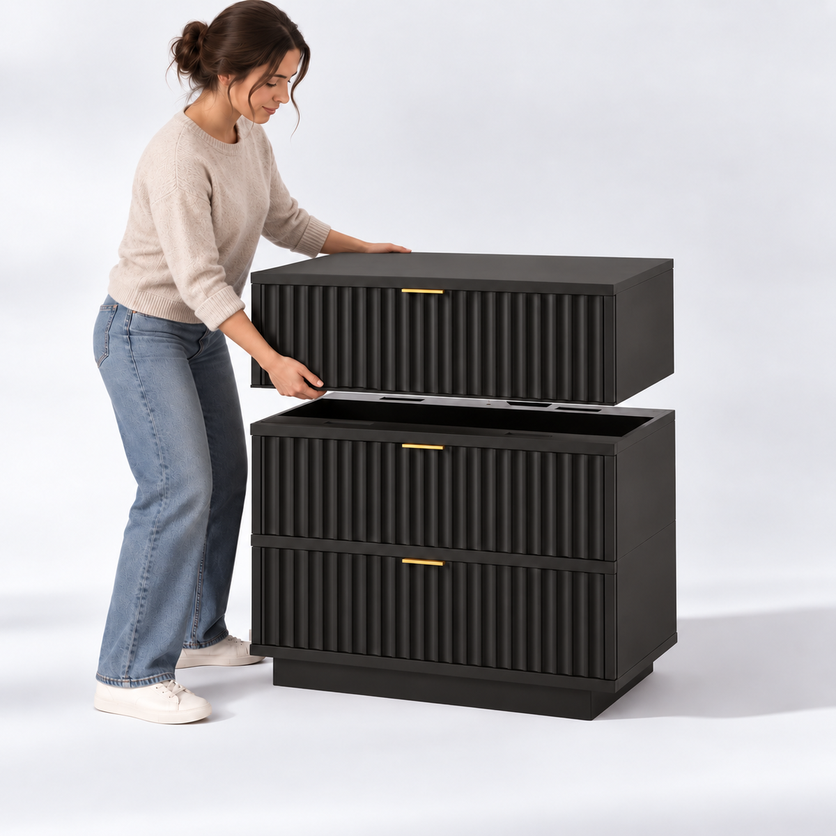 A woman places the top drawer onto a stack of two black, fluted-front drawers with gold hardware.