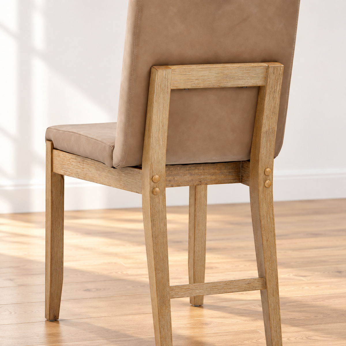 Light brown upholstered dining chair with a wooden frame seen from the back.