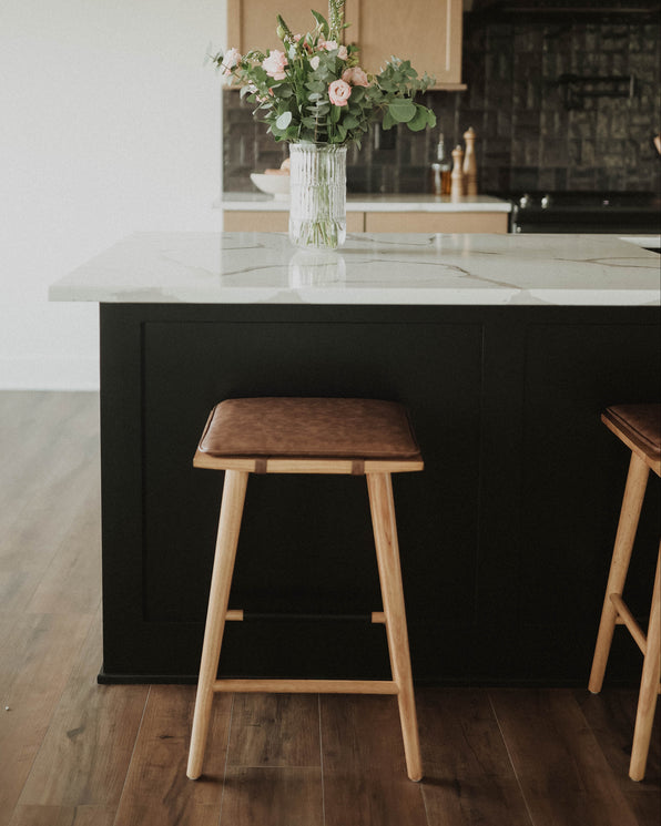 A kitchen island with a white marble countertop, a vase of pink flowers, and two wooden stools with brown cushions.