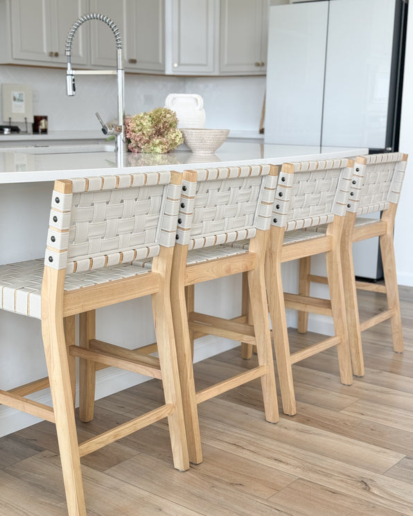 Four light wood bar stools with woven beige seats lined up along a white kitchen island.