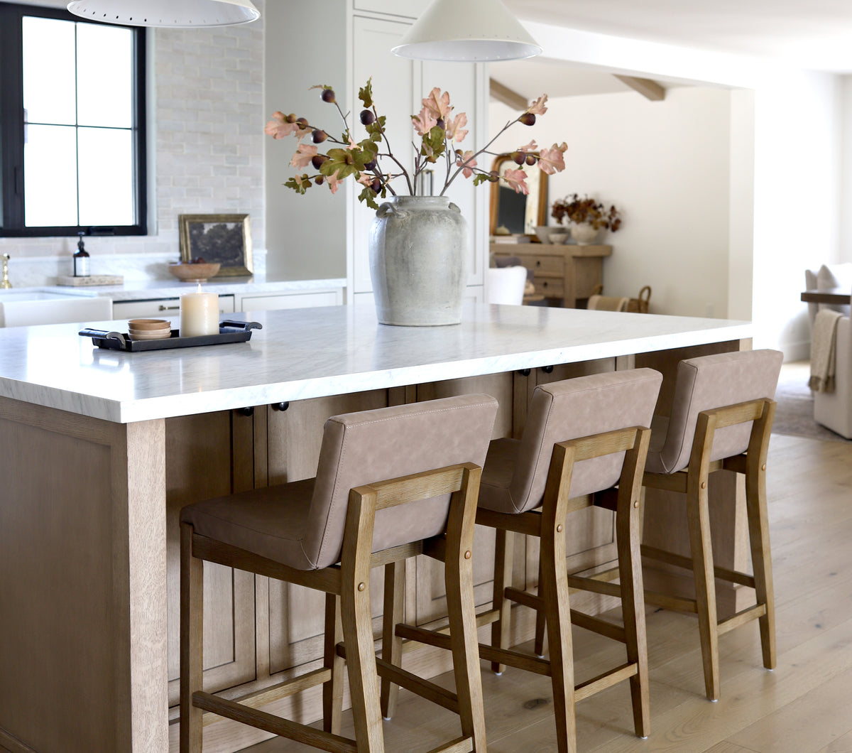 Kitchen island with three upholstered wooden bar stools and a vase of dried branches on the marble countertop.