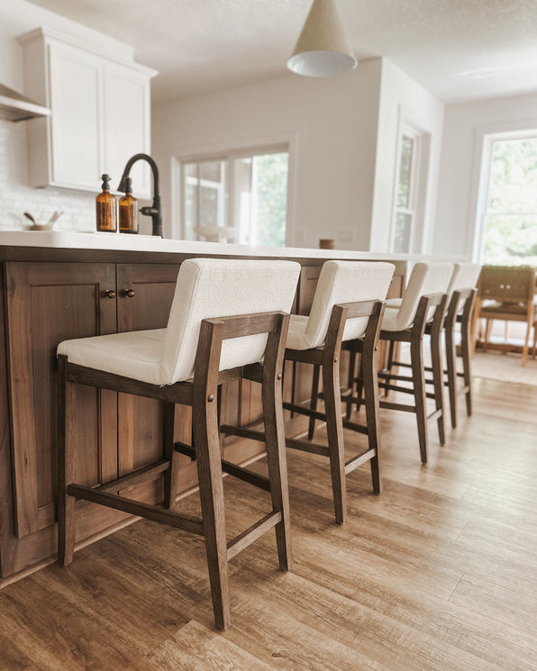 Four bar stools with white upholstered seats and dark wood frames lined up at a kitchen island.