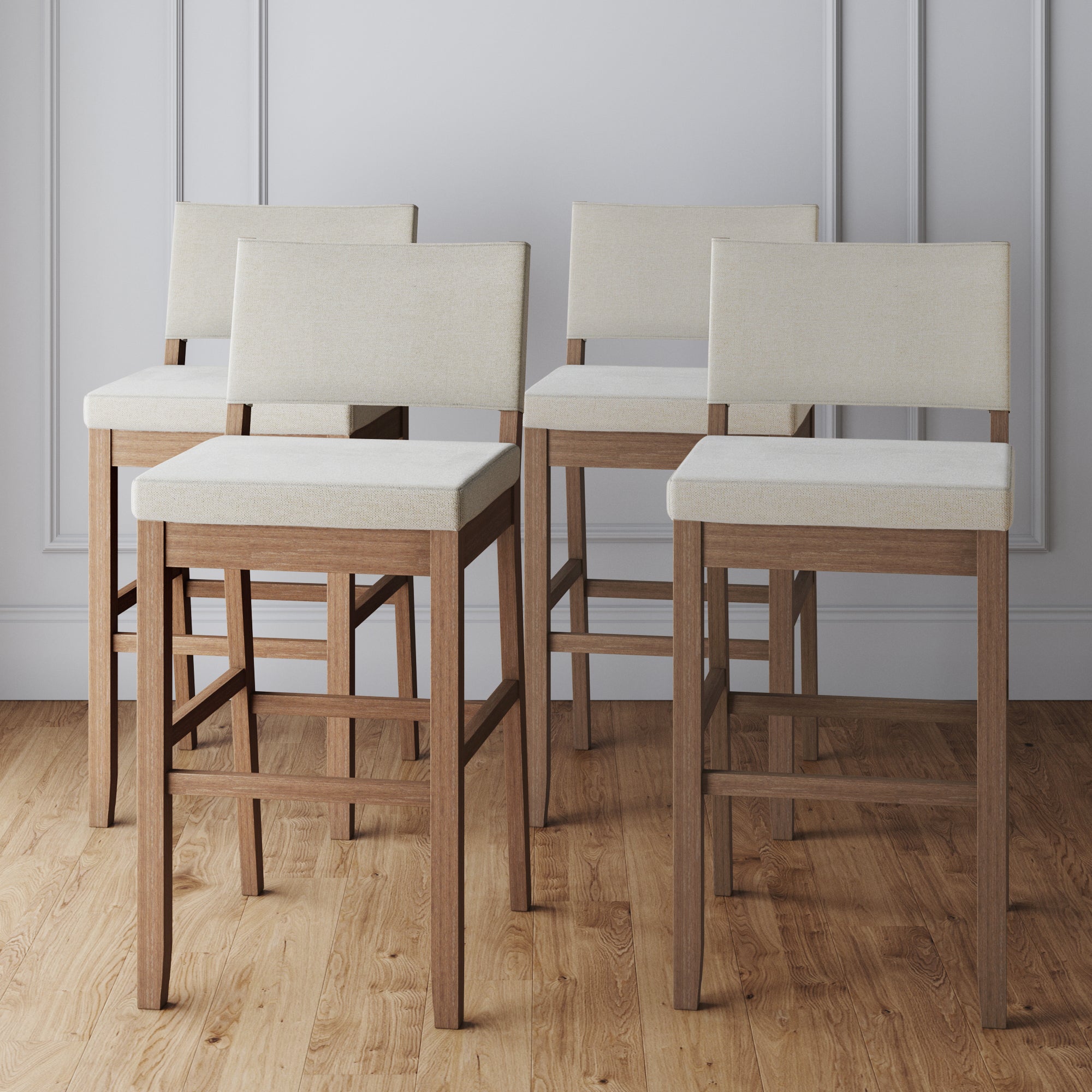 Four modern bar stools with light beige upholstered seats and backs, and wooden legs, are arranged in a staggered formation on a light wood floor against a white paneled wall.